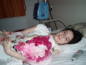 Emily Collingridge lying in a hospital bed, holding a bunch of flowers