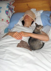 A young woman lies ill in bed with a flannel over her eyes.