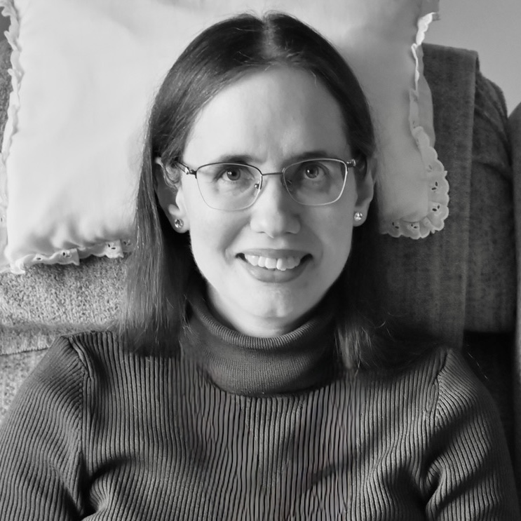 A black and white headshot of Naomi Whittingham. She is a white woman with long dark hair and glasses.